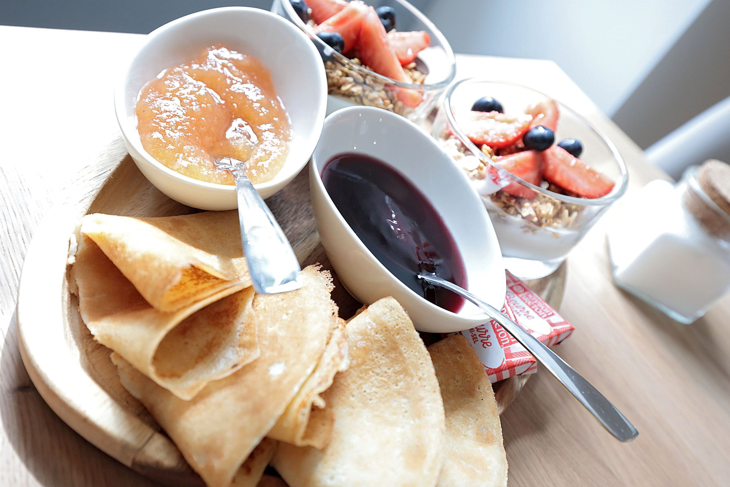 Bandeja de desayuno con panqueques, un cuenco de salsa de naranja, un cuenco de salsa oscura y un cuenco de yogur con fruta.