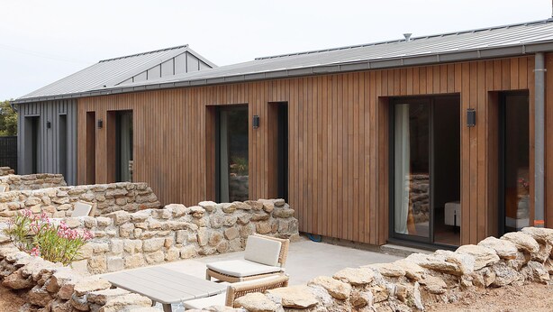 A modern building with a wooden exterior, stone walls, and a patio area with seating and a table. - Pierres Blanches (Guérande)