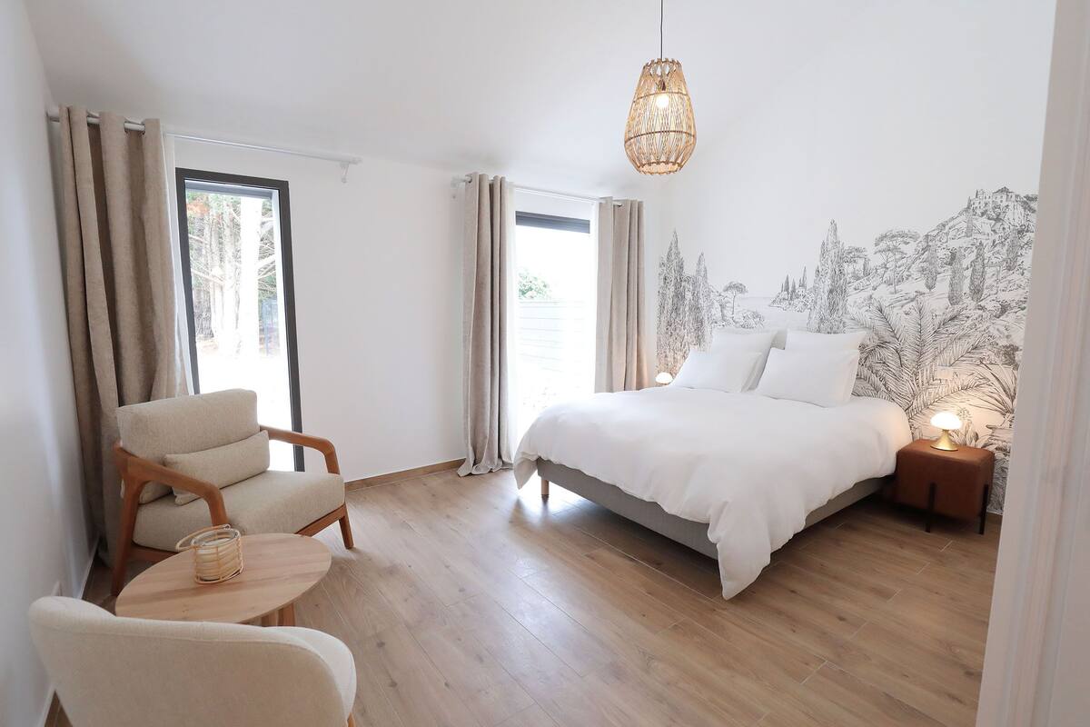 A bedroom with a bed, a chair, a small table, and a nightstand with a lamp.