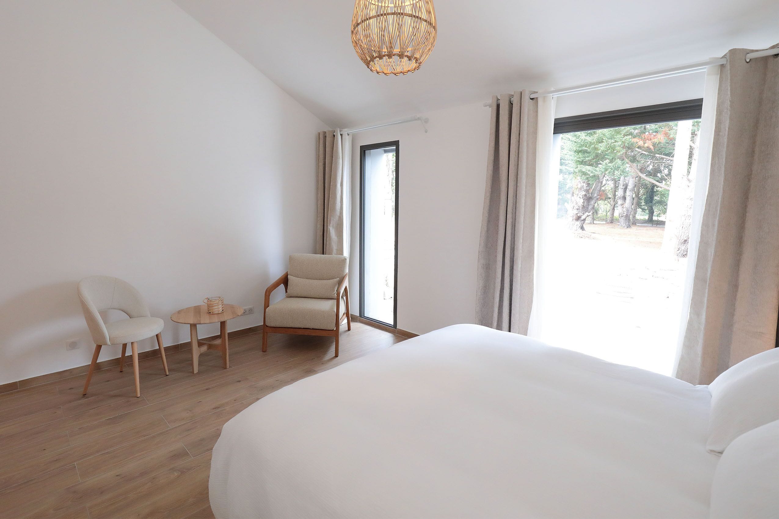 Une chambre d’hôtel avec un grand lit, une chaise, une petite table et une fenêtre avec des rideaux.