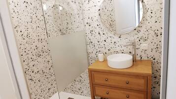 Ein Badezimmer mit einer freistehenden Dusche, einem runden Spiegel und einem Holzwaschtisch mit Waschbecken.