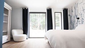 A bedroom with a large bed, a white chair, a wardrobe, and a view of trees through the window. - Pierres Blanches (Guérande)