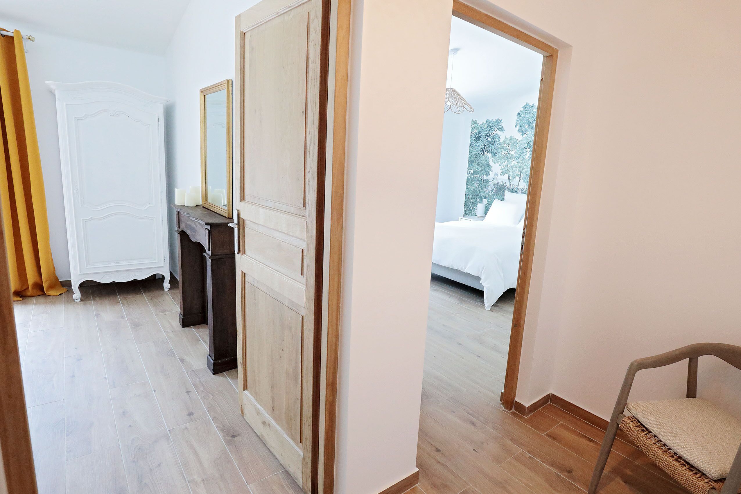Um quarto com piso de madeira, um guarda-roupa branco, um espelho e uma cama com roupa de cama branca.