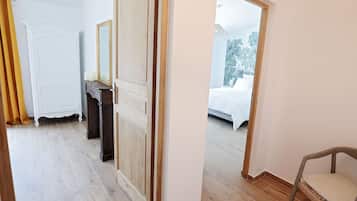 Um quarto com piso de madeira, um guarda-roupa branco, um espelho e uma cama com roupa de cama branca.