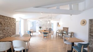A modern dining area with wooden tables and chairs, stone walls, and a view into another room. - Pierres Blanches (Guérande)