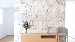 A room with a wooden console table, a grey chair, and a wall with a nature-themed wallpaper. - Pierres Blanches (Guérande)