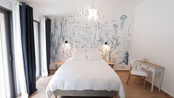 Une chambre avec un grand lit, un bureau et une chaise. Il y a une fenêtre avec des rideaux, un mur orné d’une fresque végétale et un luminaire suspendu.