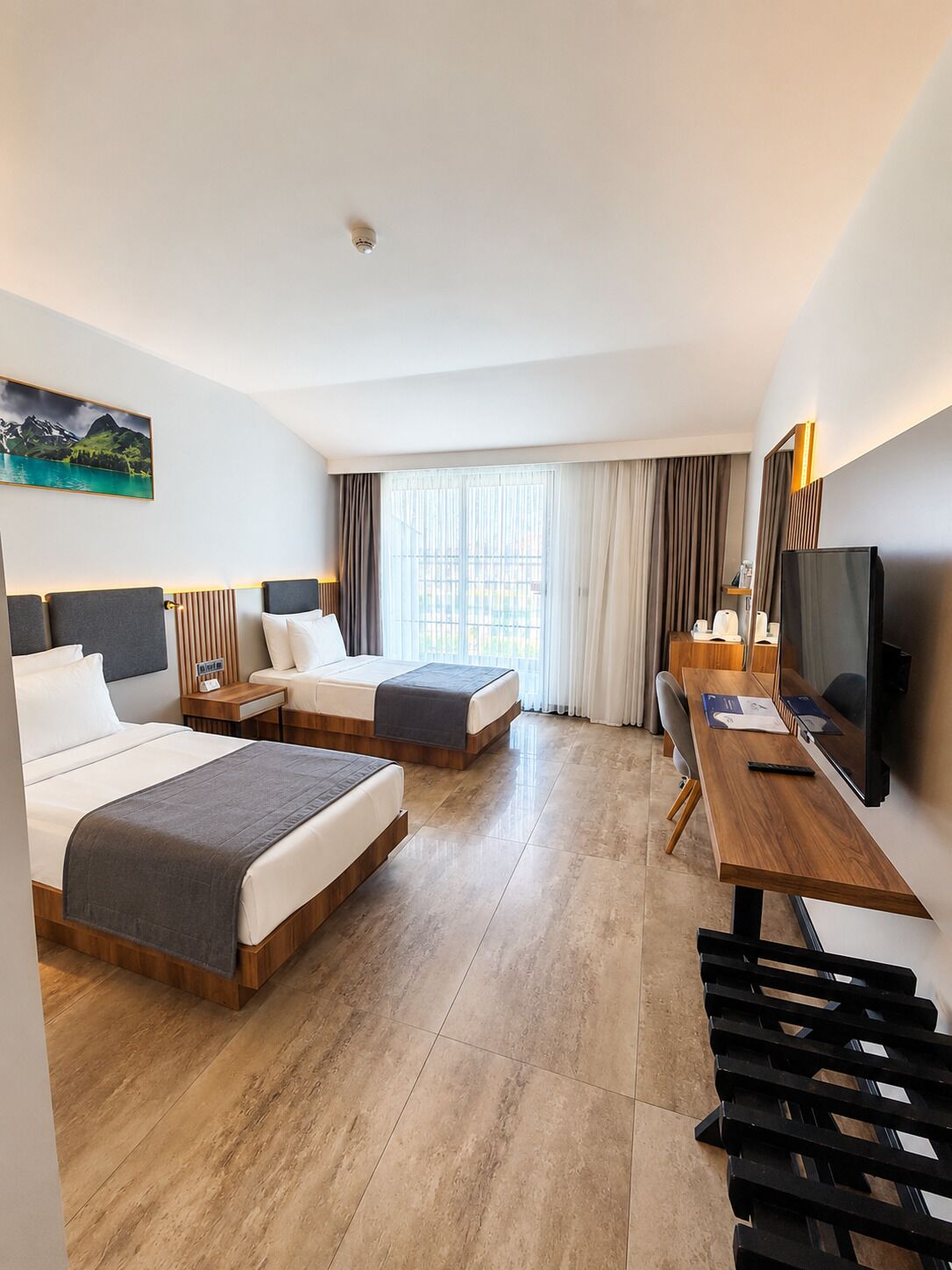 Habitación de hotel con dos camas, un escritorio, un televisor y una ventana con cortinas.