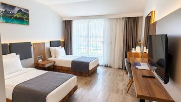 Habitación de hotel con dos camas, un escritorio, un televisor y una ventana con cortinas.