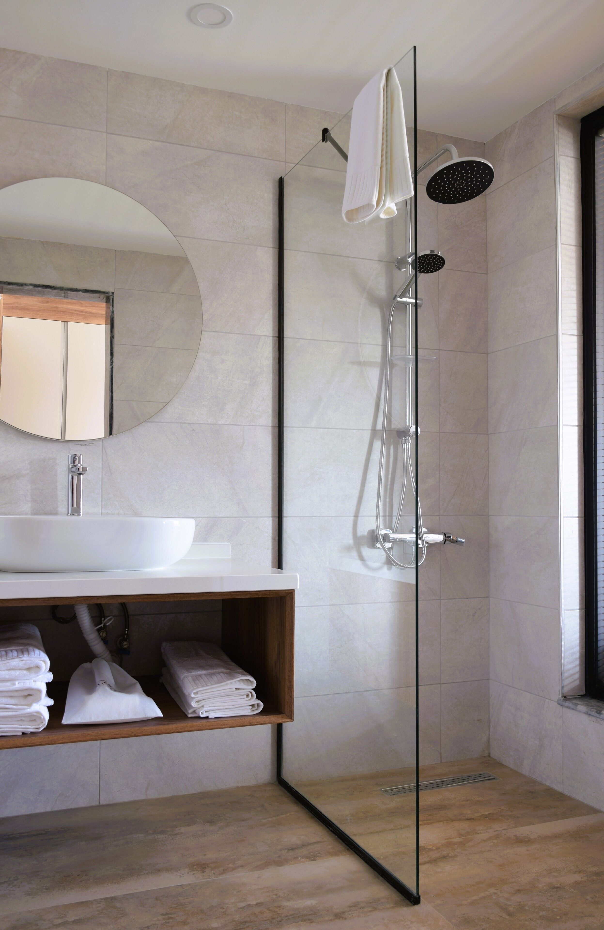 A modern bathroom with a glass-enclosed shower, a white sink, and a wooden vanity.