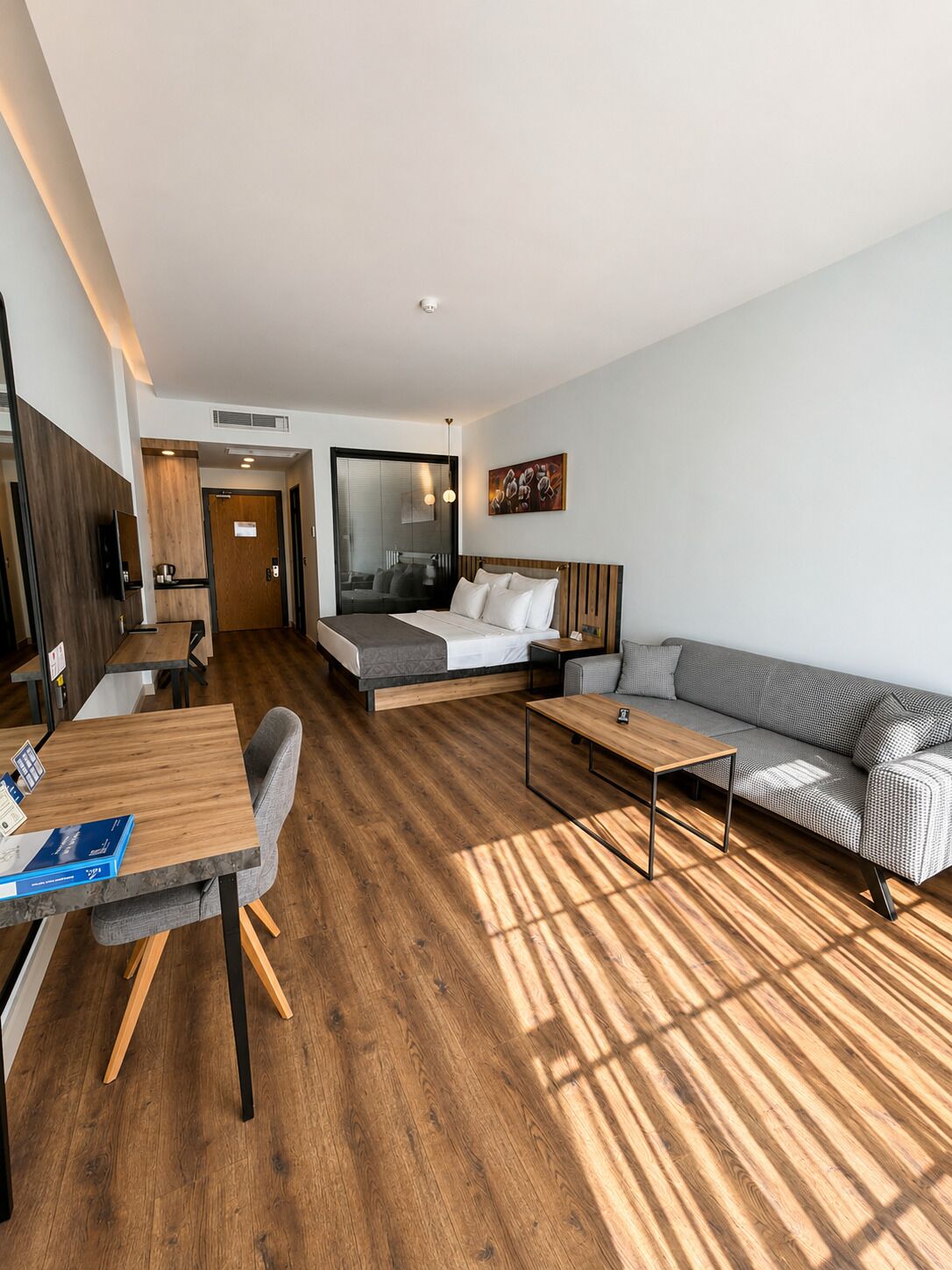 Una habitación de hotel moderna con suelo de madera, un sofá, una cama, una mesa de comedor y un televisor.