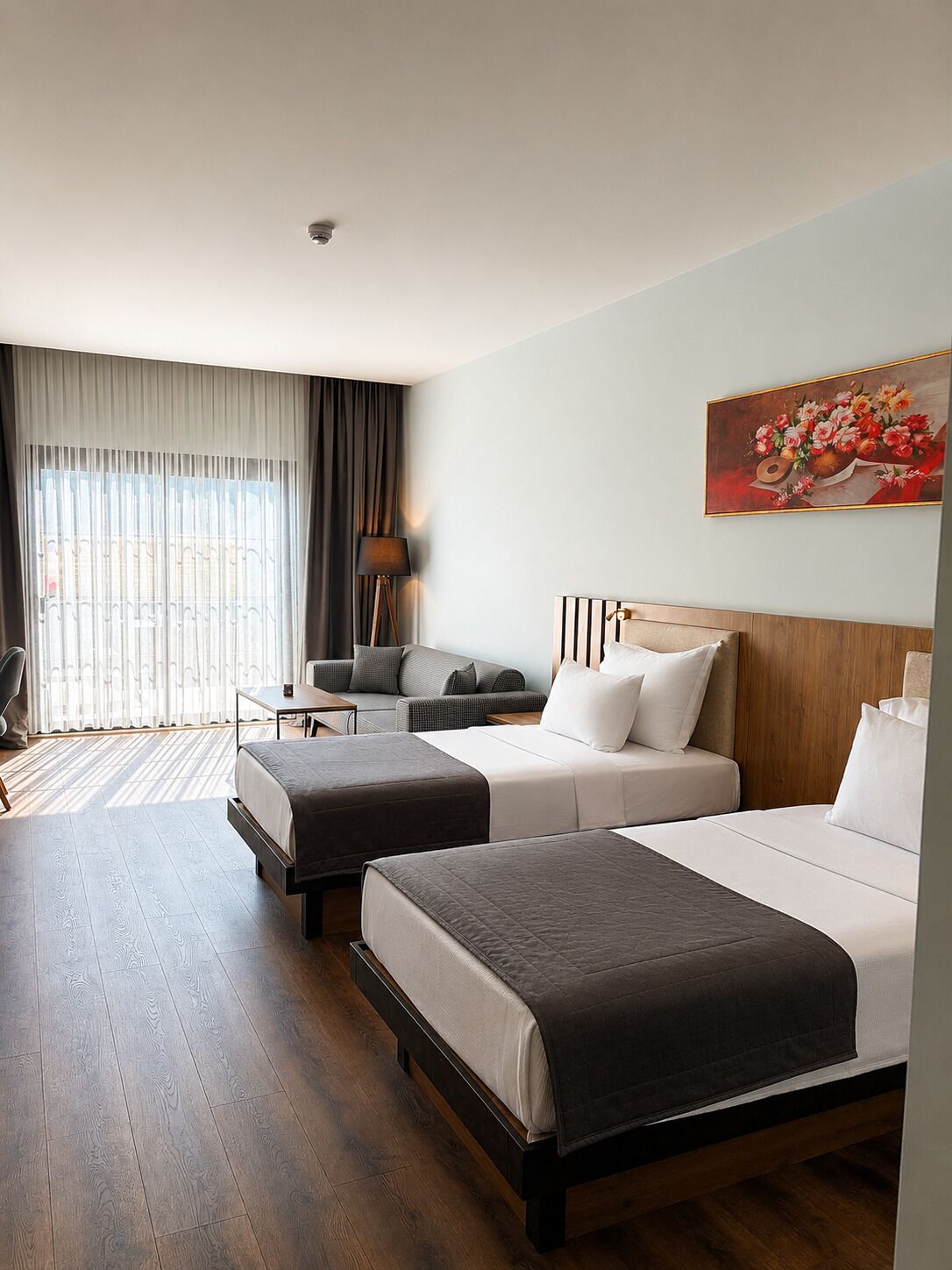 A hotel room with two beds, a sofa, a desk, and a painting on the wall.