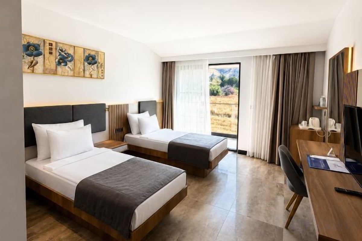 Une chambre d’hôtel avec deux lits, un bureau et une grande fenêtre avec des rideaux.