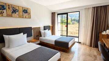 Habitación de hotel con dos camas, un escritorio, una silla, un ventanal con cortinas y una lámpara en el techo.