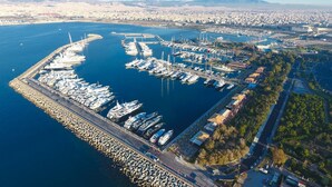 Vue aérienne d’une marina où sont amarrés de nombreux bateaux, avec une grande digue en premier plan et un paysage urbain en arrière-plan.