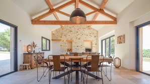 Un vaste espace dédié à la salle à manger, avec un mur en pierre, des poutres apparentes et une grande table entourée de chaises.
