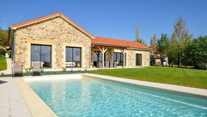 Une maison en pierre avec une piscine, de grandes fenêtres et un toit recouvert de tuiles rouges.