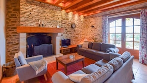 Ein gemütliches Wohnzimmer mit Steinwand, Holzbalken, Kamin, einer Couch und einem Fernseher.
