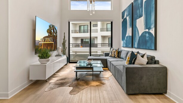 A modern living room with a glass coffee table, grey sofa, and abstract art on the wall.