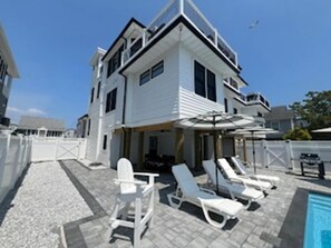 A two-story house with a pool area, including lounge chairs and umbrellas.