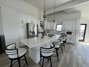 A modern kitchen with white cabinetry, a central island with bar stools, stainless steel appliances, and pendant lighting.