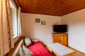 Um quarto acolhedor com teto de madeira, um sofá com almofada vermelha, uma mesa pequena e uma televisão em um armário de madeira.