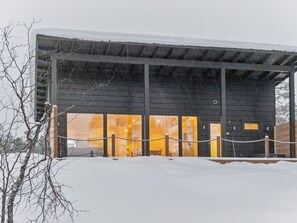 Un edificio de fachada oscura, grandes ventanales y suelo cubierto de nieve.