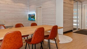 A modern meeting room with a wooden table and orange chairs, a painting on the wall, and a sliding glass door leading to a balcony.