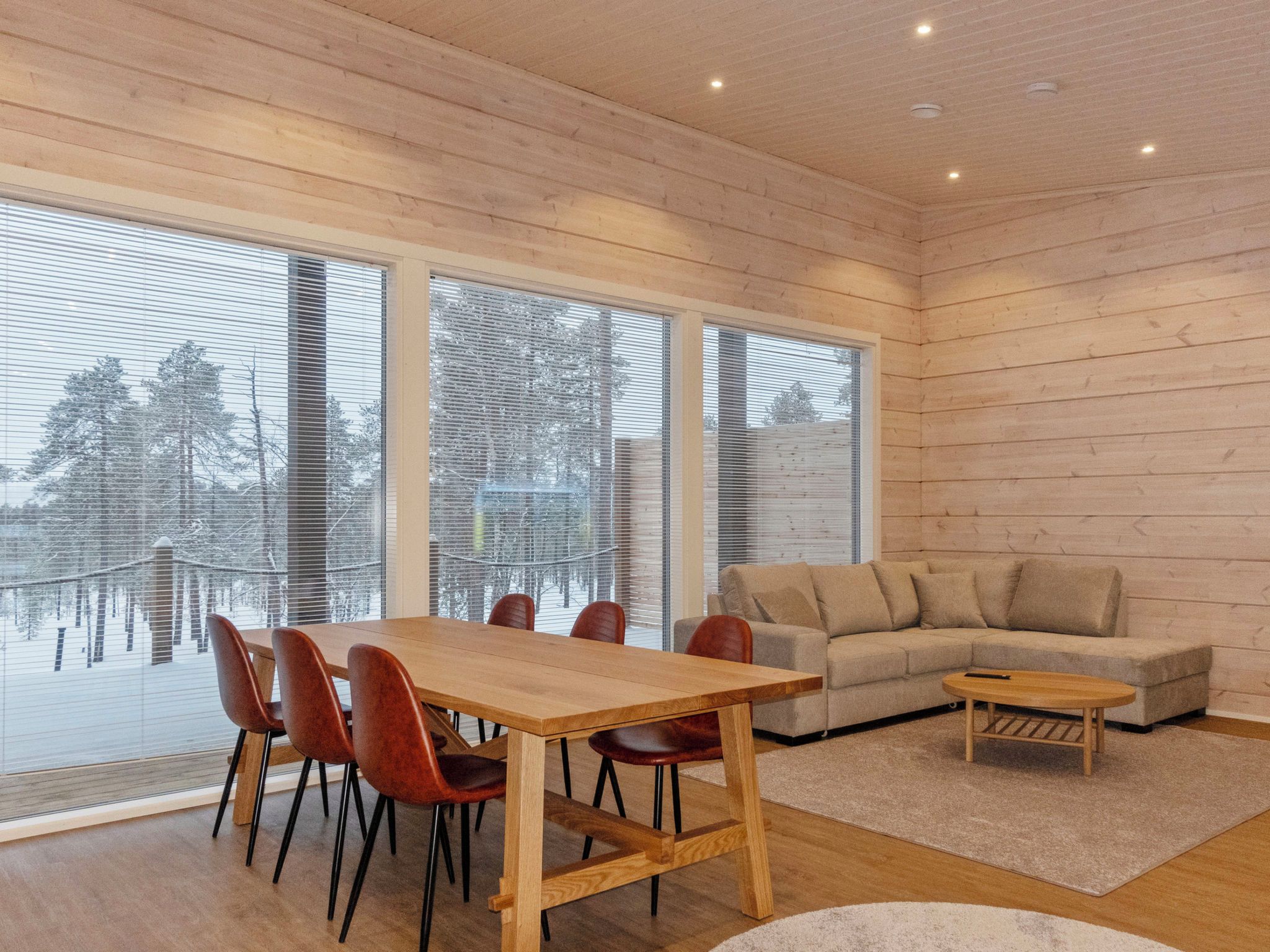 A modern interior with a wooden dining table, red chairs, a beige sofa, and large windows.