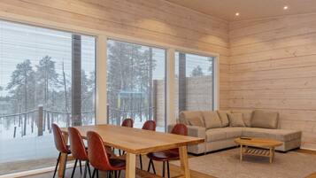 A modern interior with a wooden dining table, red chairs, a beige sofa, and large windows.