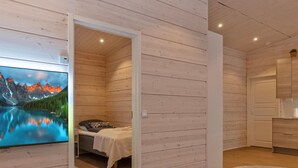 A cozy cabin room with a bed, a television displaying a mountain landscape, and a small bathroom with a mirror and sink.