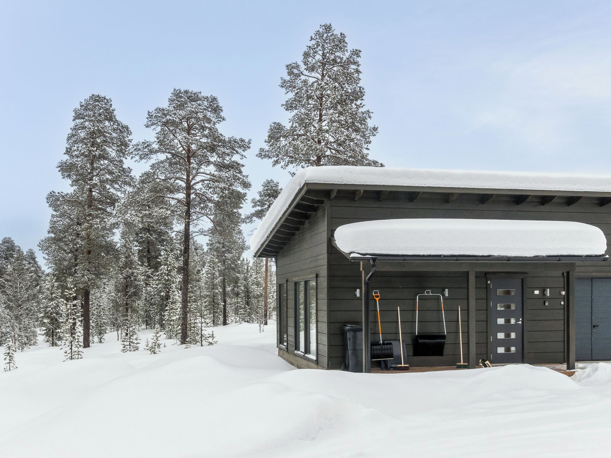 Una cabaña con techo cubierto de nieve, rodeada de altos árboles cargados de nieve.