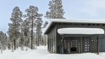 Una cabana amb un teulat cobert de neu, envoltada d'alzines carregades de neu.