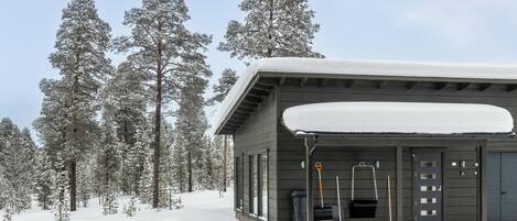 Una cabaña con techo cubierto de nieve, rodeada de altos árboles cargados de nieve.
