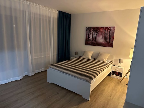 Relax in a serene space with a comfortable bed, bedside table, and a beautiful forest scene painting.