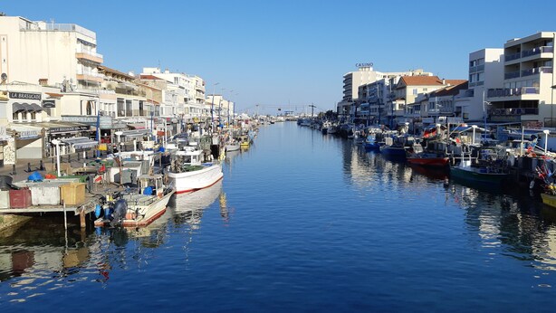 A narrow waterway lined with boats and buildings, including a casino and various shops.