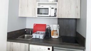A compact kitchen with a microwave, coffee maker, and dish rack.
