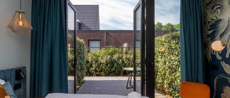 Et hotelværelse med en seng, en stol og udsigt til en bygning og have gennem en glasdør.