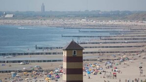 Une plage avec un phare, un rivage sablonneux et des personnes qui se promènent sur la plage.