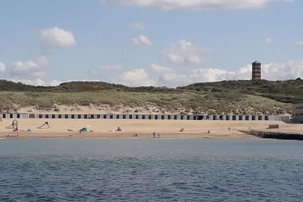 A beach with a row of beach huts, a lighthouse, and a sandy shoreline.