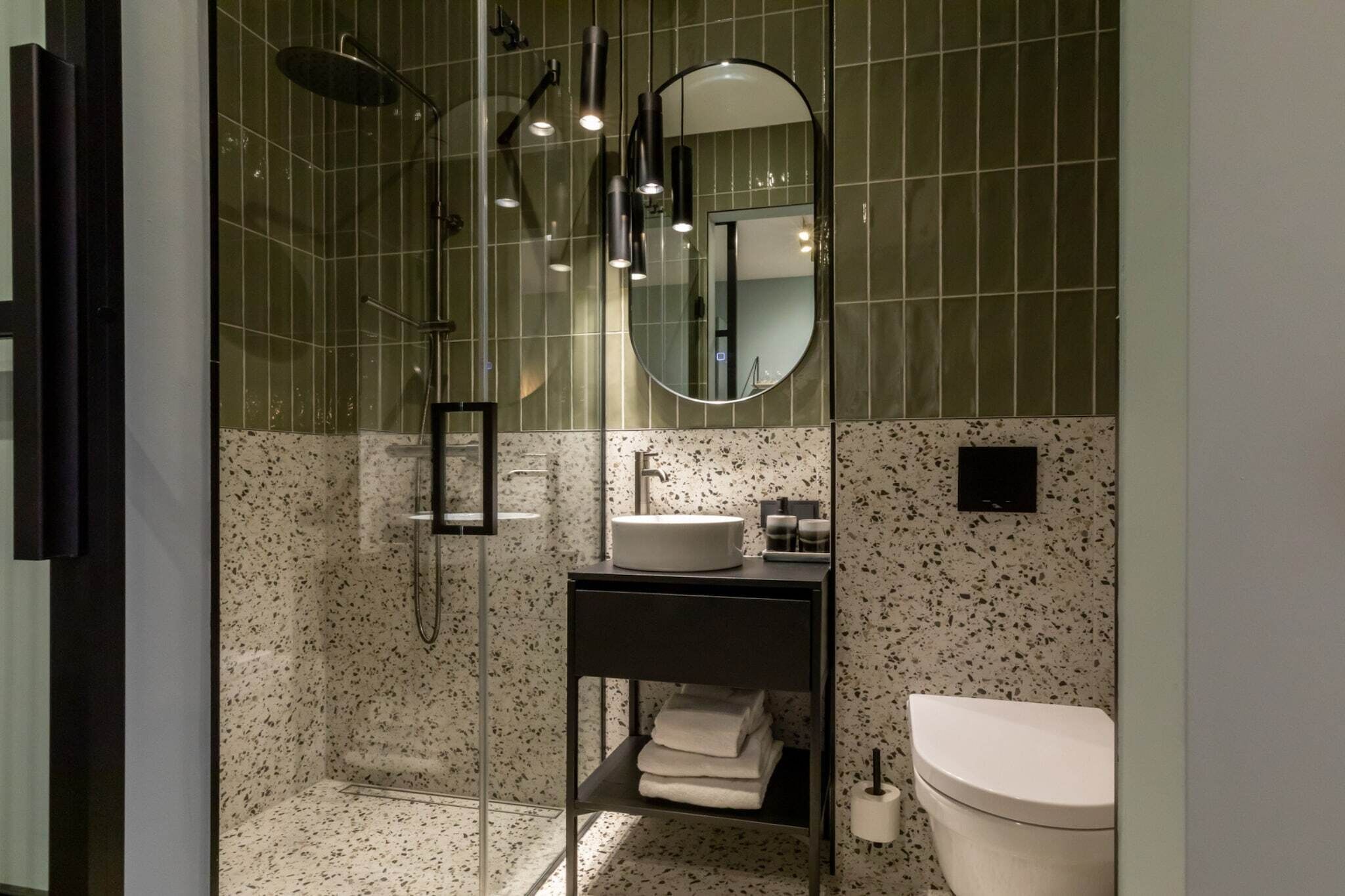 A modern bathroom with a glass-enclosed shower, a round mirror, a white sink, and a toilet.