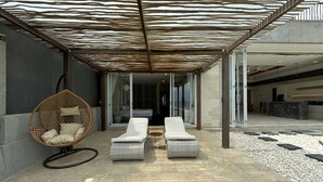 A modern outdoor lounge area with a patterned ceiling, two white lounge chairs, a wicker chair, and a stone pathway. - Beach front 2 bedroom with cinema room & infinity pool Sahadewa (Bali)