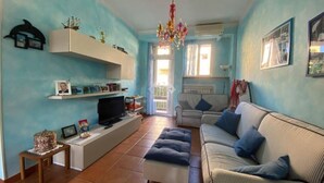 A living room with a sofa, a television, a chandelier, and a window. - Holiday home Leonida sea front close to the mountain, Marina di Carrara downtown (Marina di Carrara)