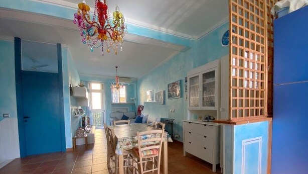 A spacious kitchen with a dining table and chairs, a chandelier, and a blue wall. - Holiday home Leonida sea front close to the mountain, Marina di Carrara downtown (Marina di Carrara)