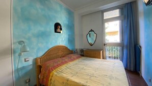 A bedroom with a bed, a nightstand, a wall-mounted lamp, a window with curtains, and a door. - Holiday home Leonida sea front close to the mountain, Marina di Carrara downtown (Marina di Carrara)