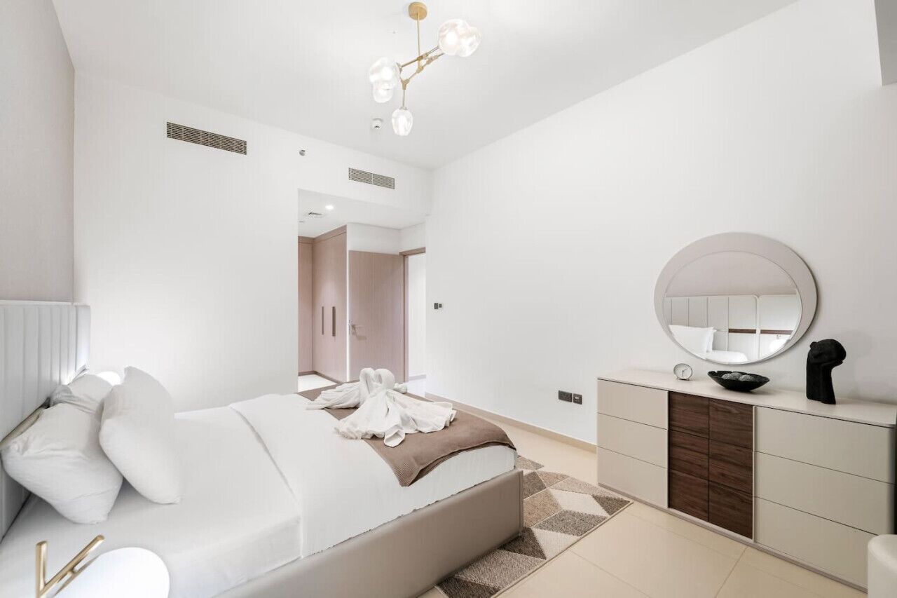 A modern bedroom with a large bed, a bedside table, a mirror, and a wardrobe.
