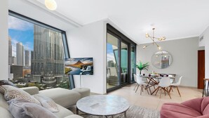 A modern living room with a city view, a dining area with a round table, and a large window. - Downtown 3BR | Sleeps 9 | Balcony, Full Kitchen, Near Metro (Downtown)