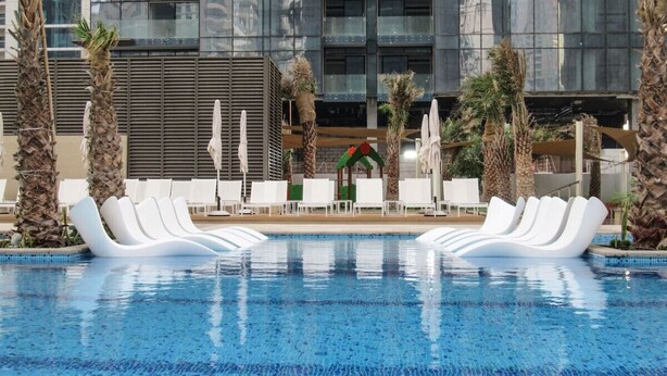 A swimming pool with white lounge chairs and palm trees, surrounded by a modern building with large windows. - Luxury 3BR at Marina Gate | Stunning Sea Views, Pool, Gym & Prime Location (Marina)