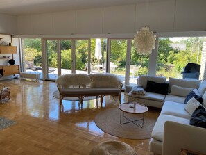 A spacious living room with a sofa, a round coffee table, and a bench. Large windows provide a view of the outdoors. - Cottage with 400 m to the water and the marina (Østerby Havn)