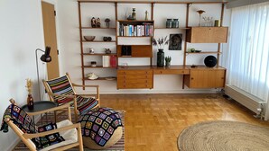 A cozy living room with a wooden bookshelf, a striped chair, a round rug, and a wooden desk.
